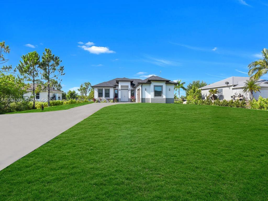 A single-story house with a white exterior and a long driveway sits on a lawn — 4210 58th Ave NE, Naples FL 34120, NAPLES, FL