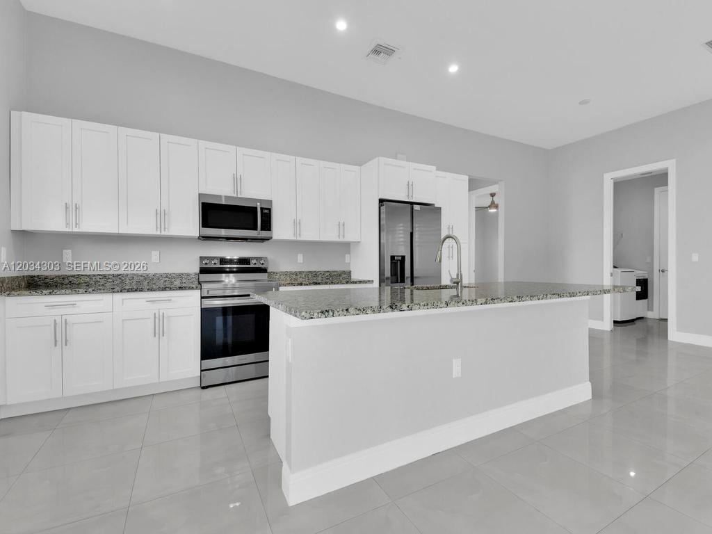 A modern kitchen features white cabinets, stainless steel appliances, granite countertops, and light tile flooring — 4210 58th Ave NE, Naples FL 34120, NAPLES, FL