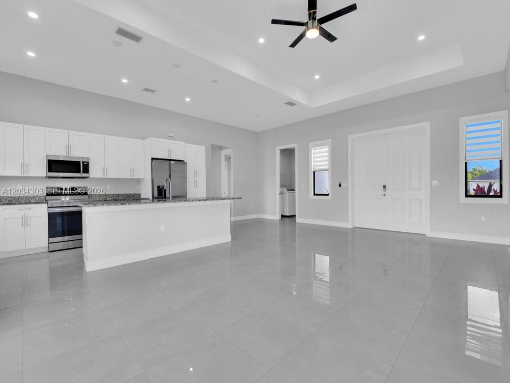A modern, open-concept kitchen features white cabinetry, granite countertops, and light-colored tile flooring — 4210 58th Ave NE, Naples FL 34120, NAPLES, FL