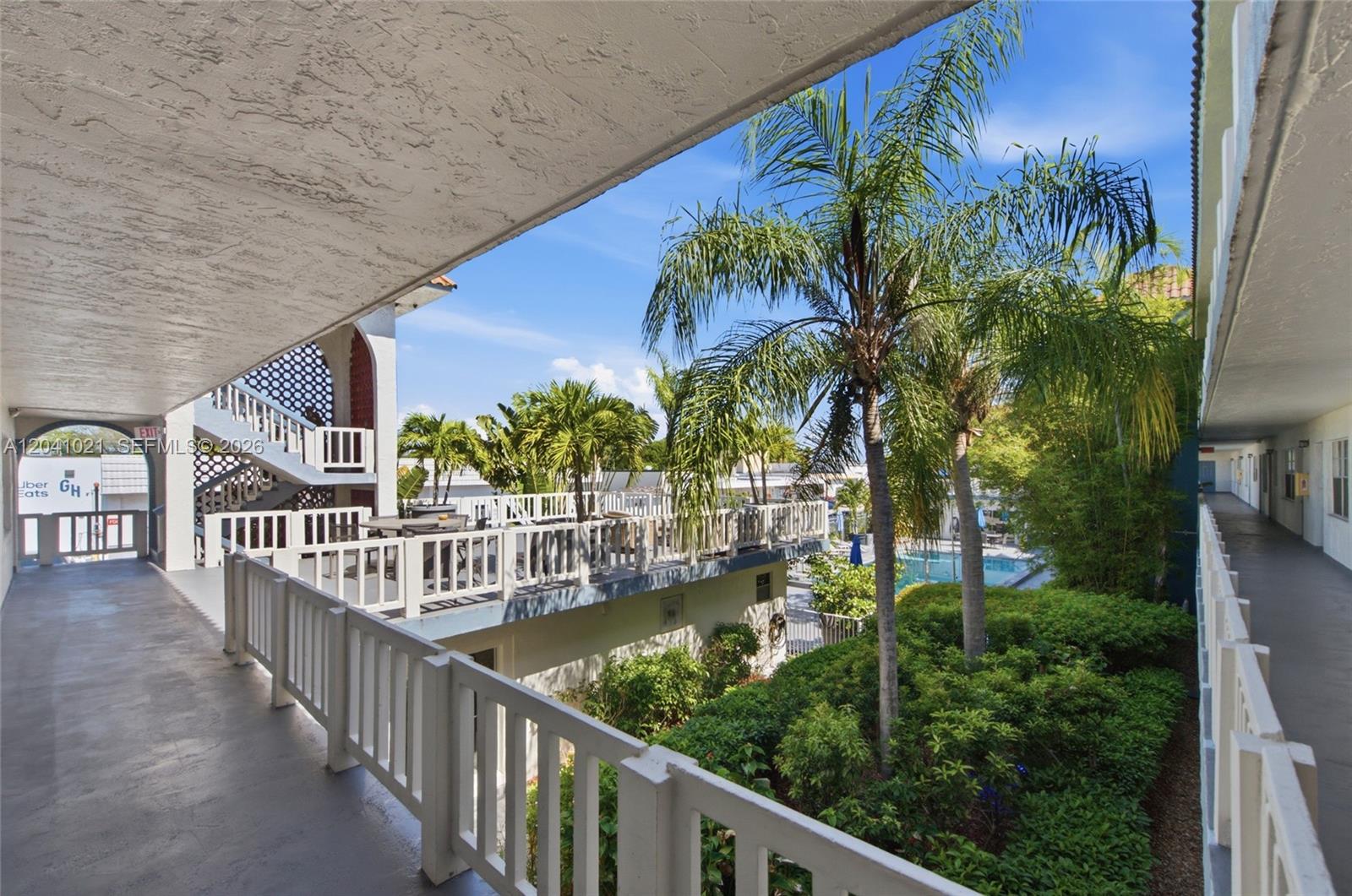 An outdoor walkway overlooks a courtyard with a swimming pool, palm trees, and white railings — FORT LAUDERDALE, FL