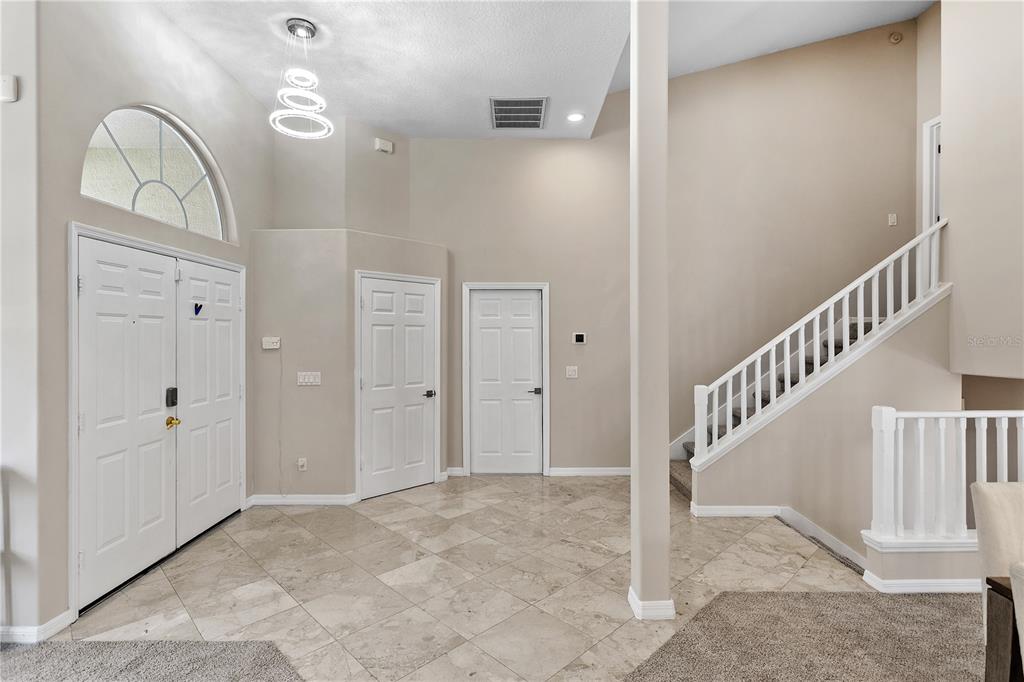 A high-ceilinged foyer features tile flooring, a staircase with white railings, and a double-door entrance — 690 OAK HOLLOW WAY, ALTAMONTE SPRINGS, FL