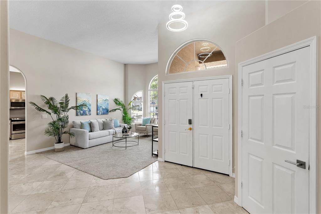 A bright living room features high ceilings, tile flooring, a sofa, and a front entryway — 690 OAK HOLLOW WAY, ALTAMONTE SPRINGS, FL
