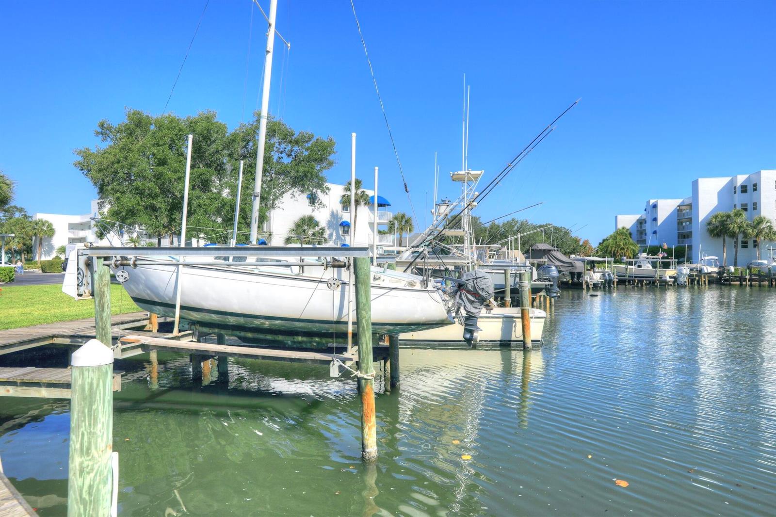 A sailboat sits on a boat lift in a marina next to white apartment buildings — SEBASTIAN, FL