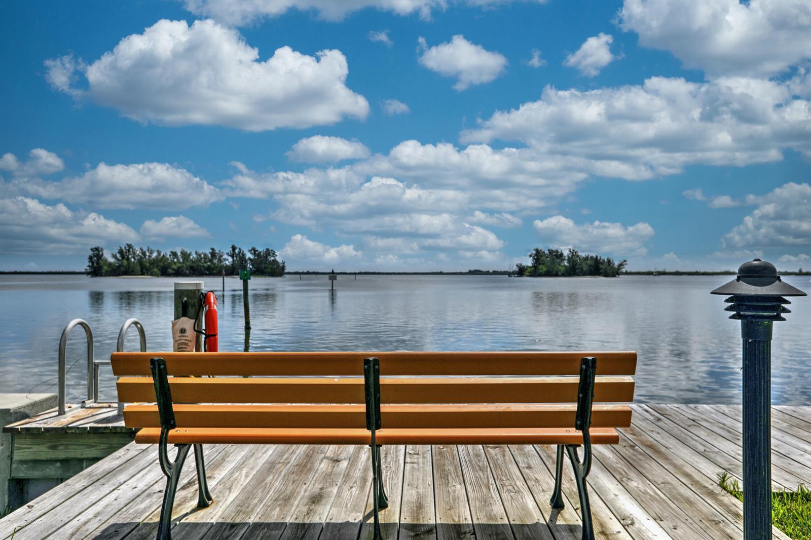 A wooden bench sits on a dock overlooking a calm body of water and islands — SEBASTIAN, FL