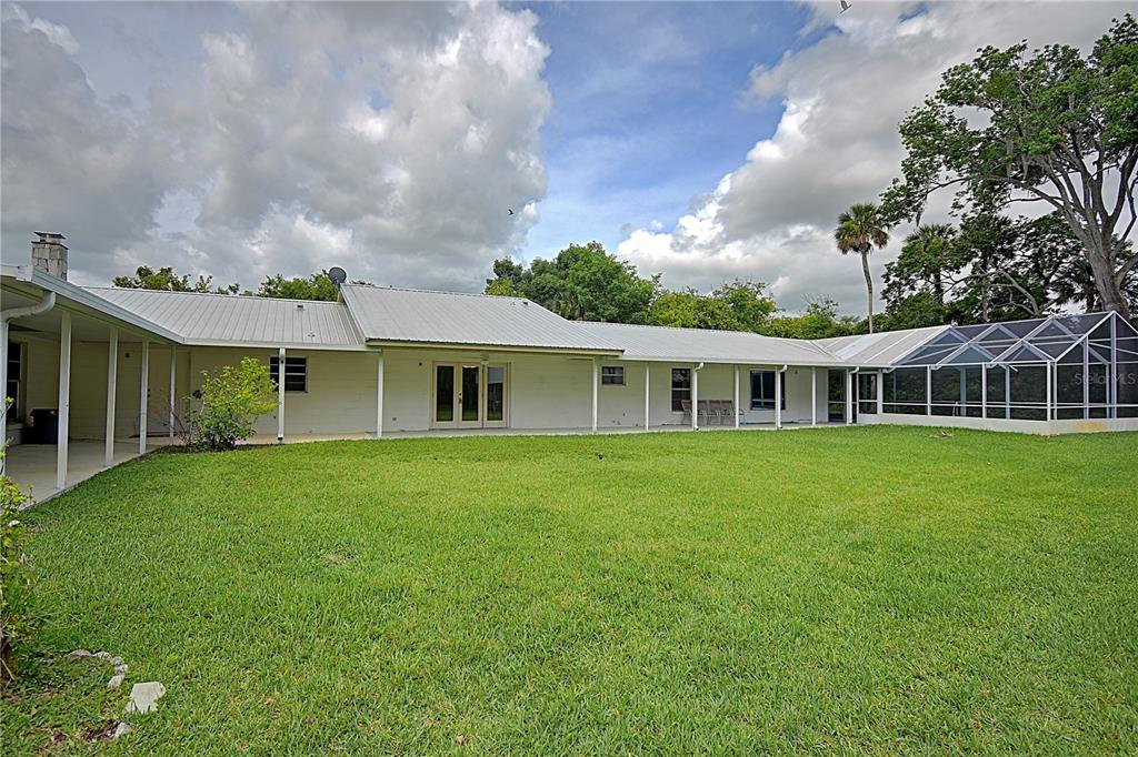 The rear exterior of a white, single-story house features a metal roof and screened-in patio — 3289 S NOVA ROAD, PORT ORANGE, FL