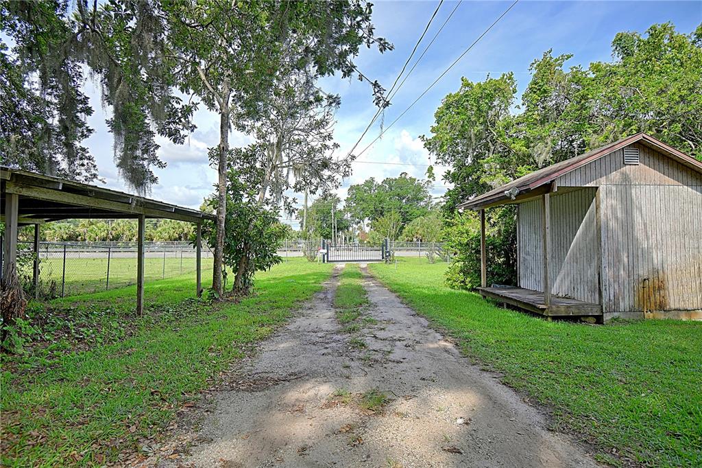 A dirt driveway leads toward a gated entrance between a wooden shed and a carport — 3289 S NOVA ROAD, PORT ORANGE, FL