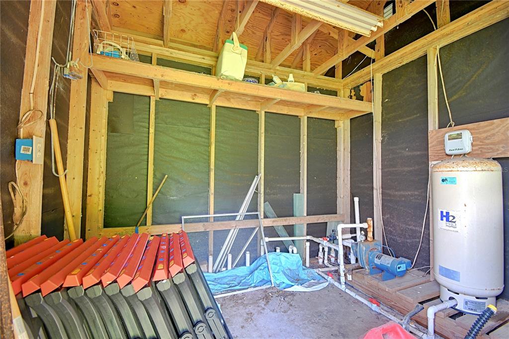 An unfinished utility shed contains a water pressure tank, a pump, and stacked folding chairs — 3289 S NOVA ROAD, PORT ORANGE, FL