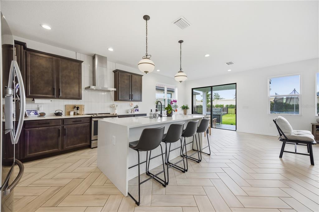 A modern kitchen features dark wood cabinetry, a white quartz island, and herringbone tile flooring — 8326 ABALONE LOOP, PARRISH, FL