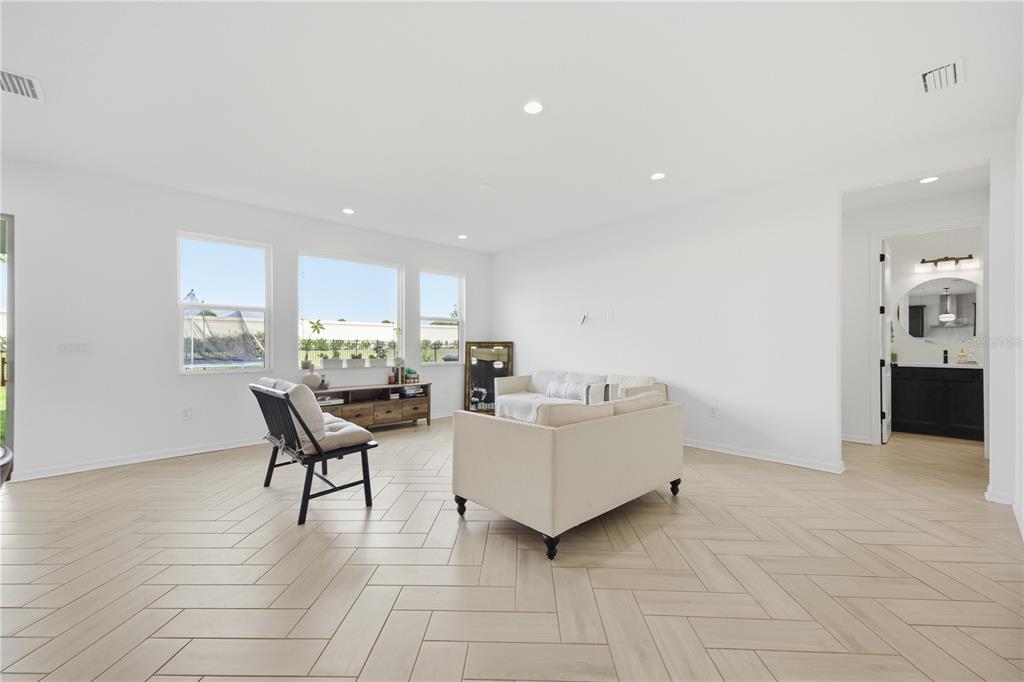 A living room with white walls, light wood-look herringbone floors, and a beige sofa — 8326 ABALONE LOOP, PARRISH, FL