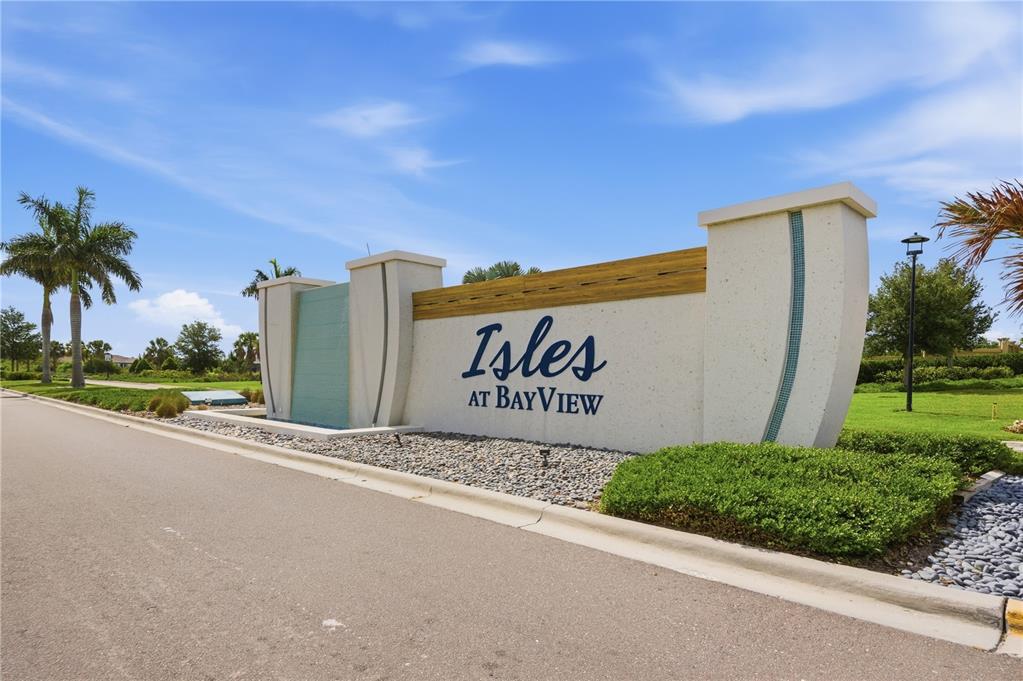 A modern stone monument sign for Isles at BayView stands beside a paved road — 8326 ABALONE LOOP, PARRISH, FL