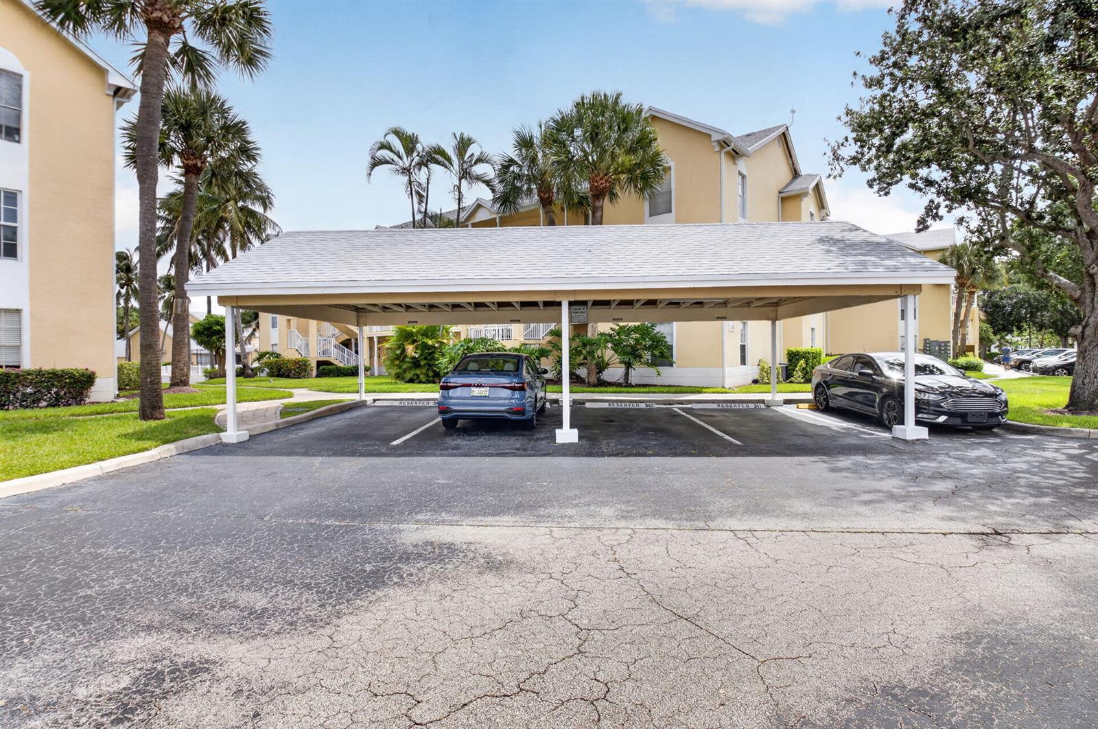 A covered parking structure with two cars parked in front of a multi-story apartment building — 6339 La Costa Drive # D, Boca Raton FL 33433, BOCA RATON, FL