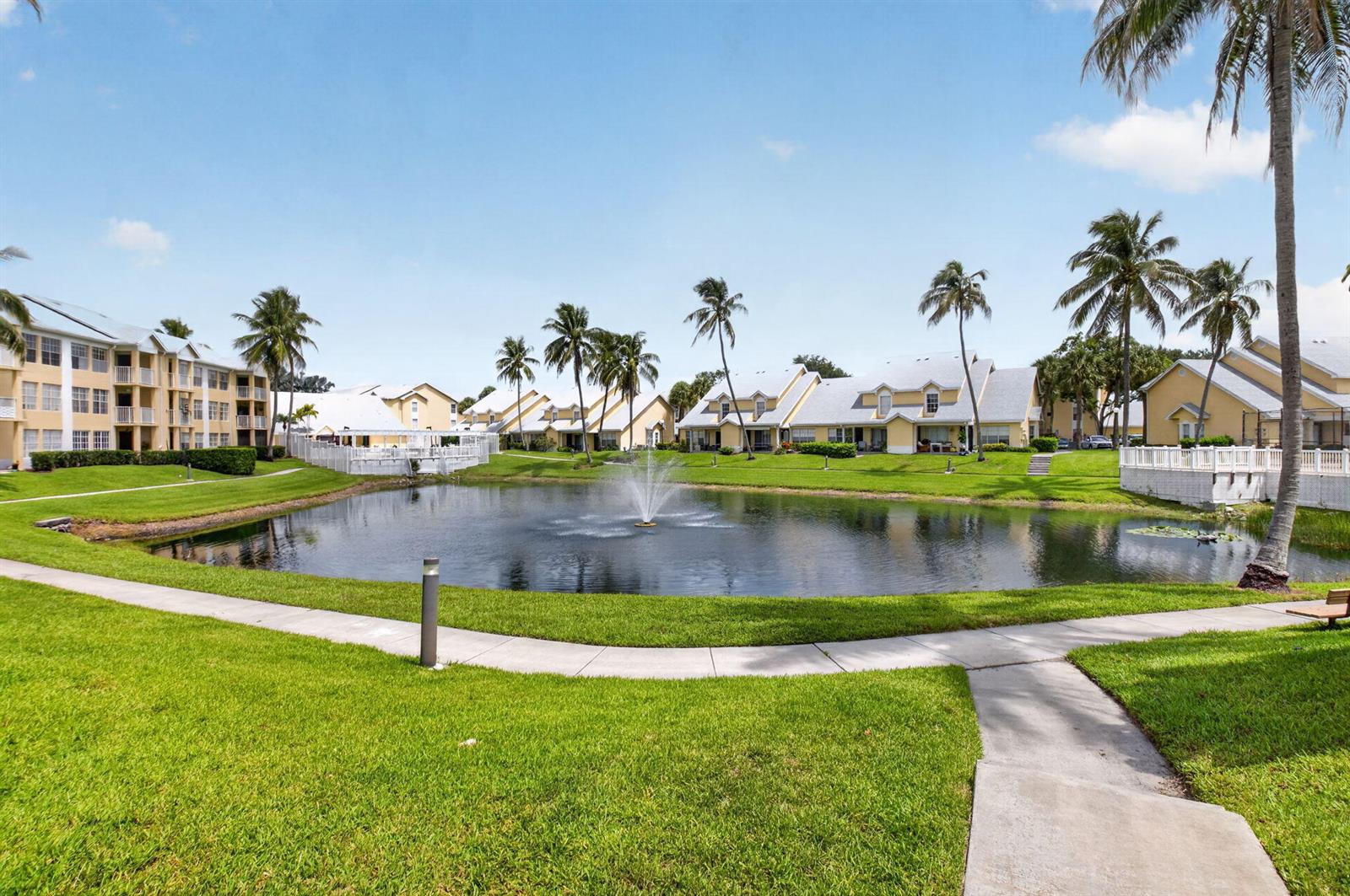 A pond with a fountain sits in front of multi-story apartment buildings and palm trees — 6339 La Costa Drive # D, Boca Raton FL 33433, BOCA RATON, FL