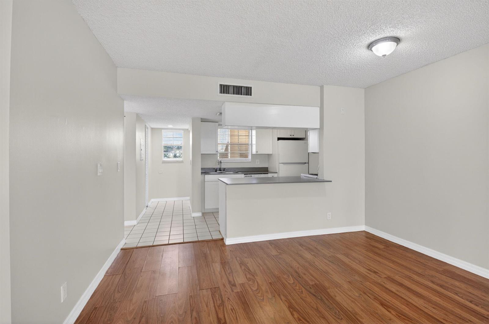 A living area with wood-look flooring opens to a kitchen featuring white cabinets and tile — 6339 La Costa Drive # D, Boca Raton FL 33433, BOCA RATON, FL