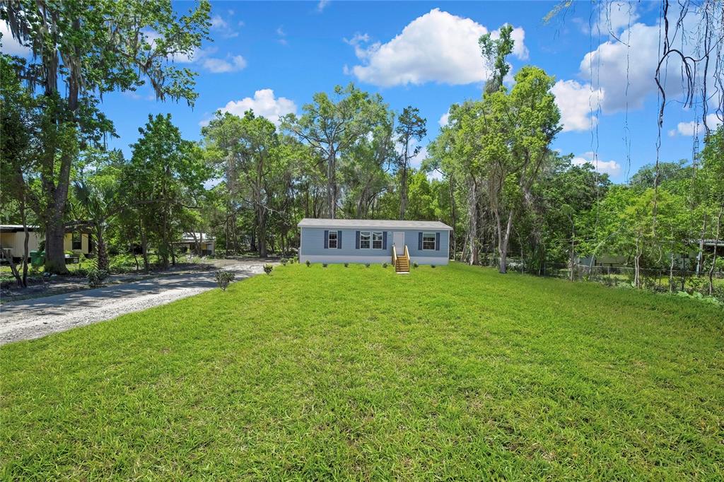 A light blue manufactured home with dark shutters sits on a grassy lot with trees — 4540 N WINCHESTER TERRACE, HERNANDO, FL
