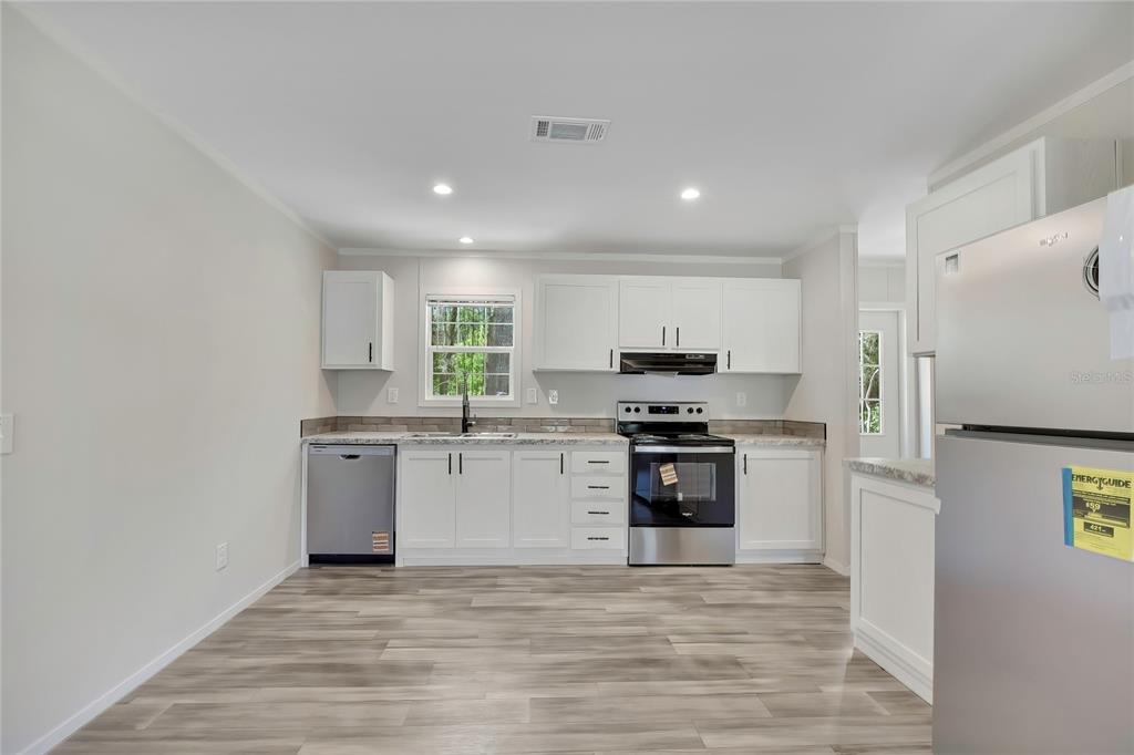 A kitchen features white cabinets, stainless steel appliances, and light wood-look flooring — 4540 N WINCHESTER TERRACE, HERNANDO, FL