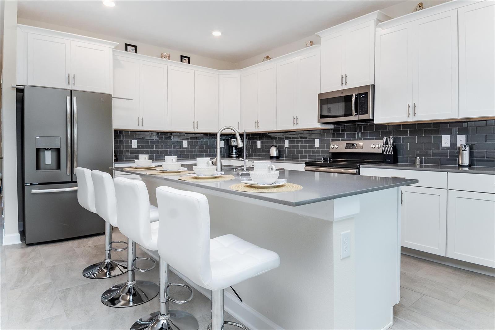 A modern kitchen features white cabinetry, a gray island with bar stools, and dark backsplash — 8936 Cabot Cliffs, Davenport FL 33896, DAVENPORT, FL
