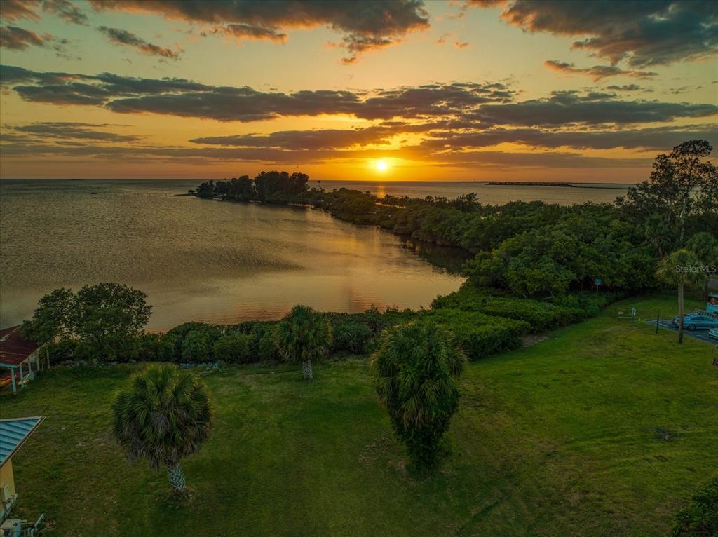 An aerial view of a grassy lawn leading to a coastal shoreline at sunset — 1725 GULF ROAD, TARPON SPRINGS, FL