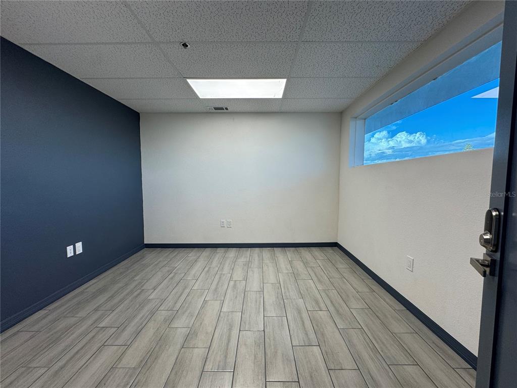 An empty office room features light wood-look tile flooring, a dark accent wall, and a window — 1460 S MCCALL ROAD UNIT A2, ENGLEWOOD, FL