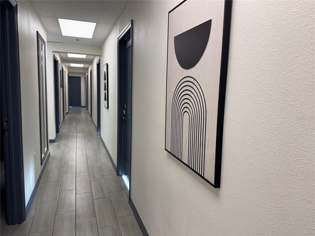 A long hallway features gray wood-look tile flooring, white walls, and framed abstract art — 1460 S MCCALL ROAD UNIT A2, ENGLEWOOD, FL