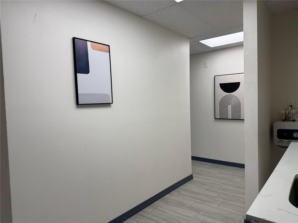 A hallway with light-colored walls, wood-look tile flooring, and two pieces of abstract wall art — 1460 S MCCALL ROAD UNIT A2, ENGLEWOOD, FL