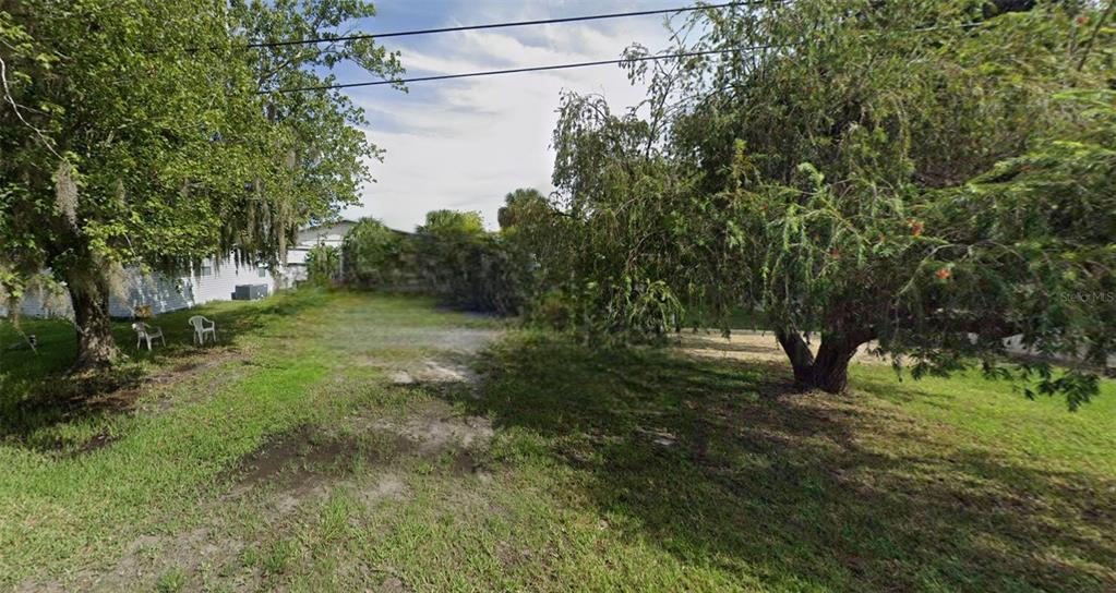 A grassy, tree-lined vacant lot sits between residential properties under a cloudy sky — 6711 BUTCH STREET, PORT RICHEY, FL