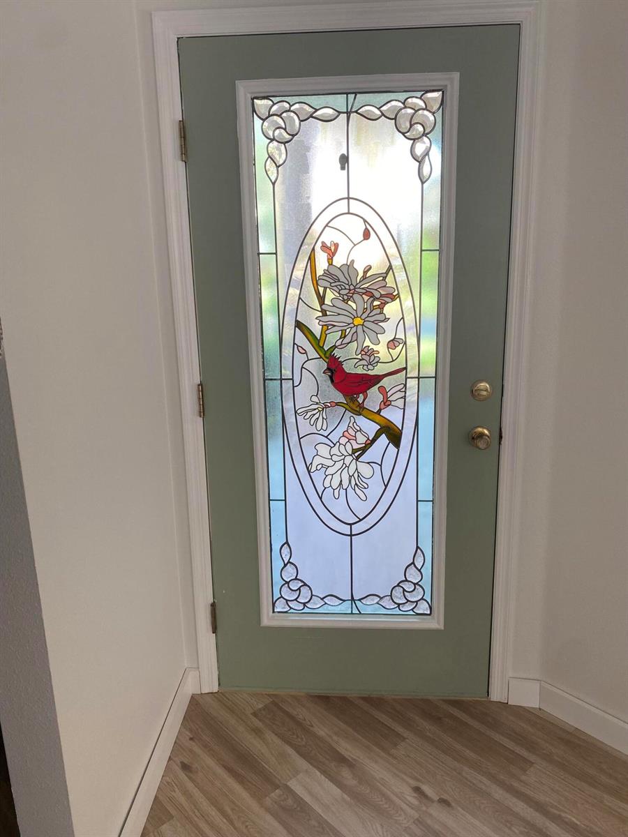 A sage green front door features a decorative stained glass insert with a cardinal design — 176 Cape Florida Drive, FL 34759, FL