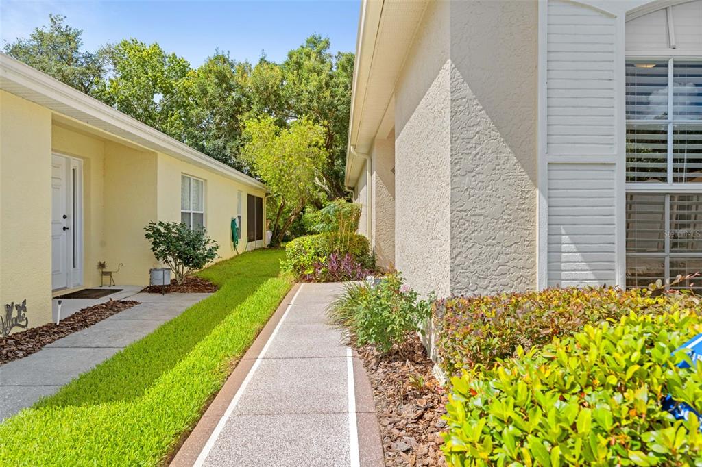 A concrete walkway leads between two light-colored houses with green landscaping and trees — 11132 HEATHROW AVENUE, SPRING HILL, FL