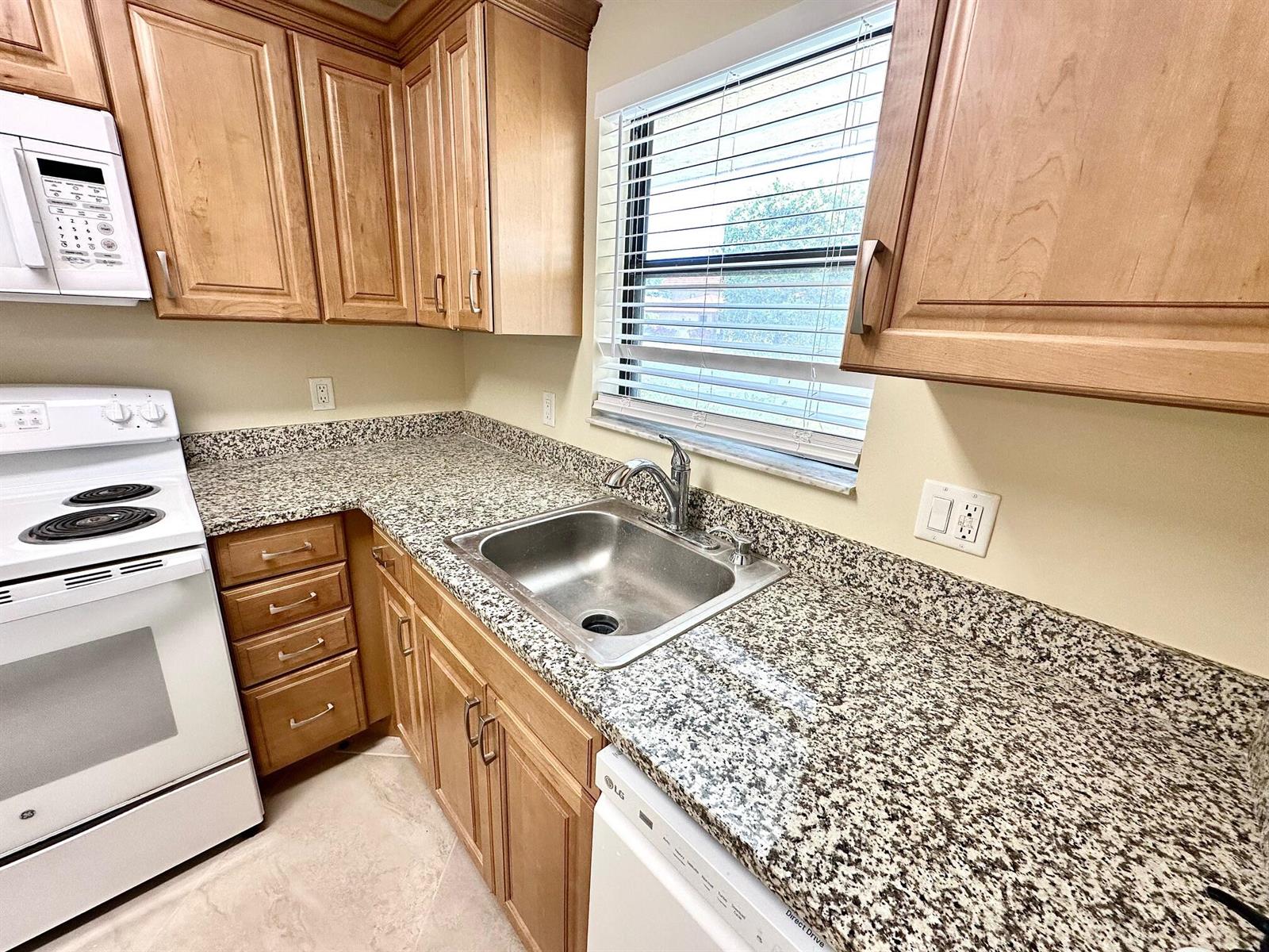 A kitchen features light wood cabinets, granite countertops, a stainless steel sink, and white appliances — 21904 Lake Forest Circle # 101, Boca Raton FL 33433, BOCA RATON, FL