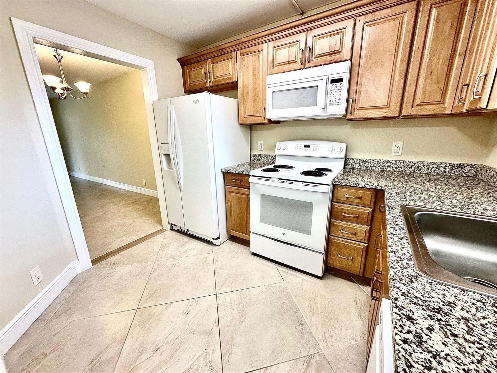 A kitchen features wood cabinets, white appliances, granite countertops, and light-colored tile flooring — 21904 Lake Forest Circle # 101, Boca Raton FL 33433, BOCA RATON, FL