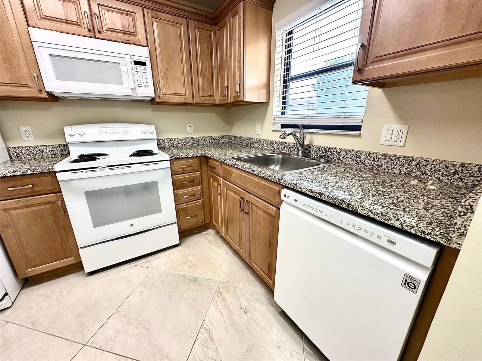 A kitchen features light wood cabinets, granite countertops, white appliances, and tiled flooring — 21904 Lake Forest Circle # 101, Boca Raton FL 33433, BOCA RATON, FL
