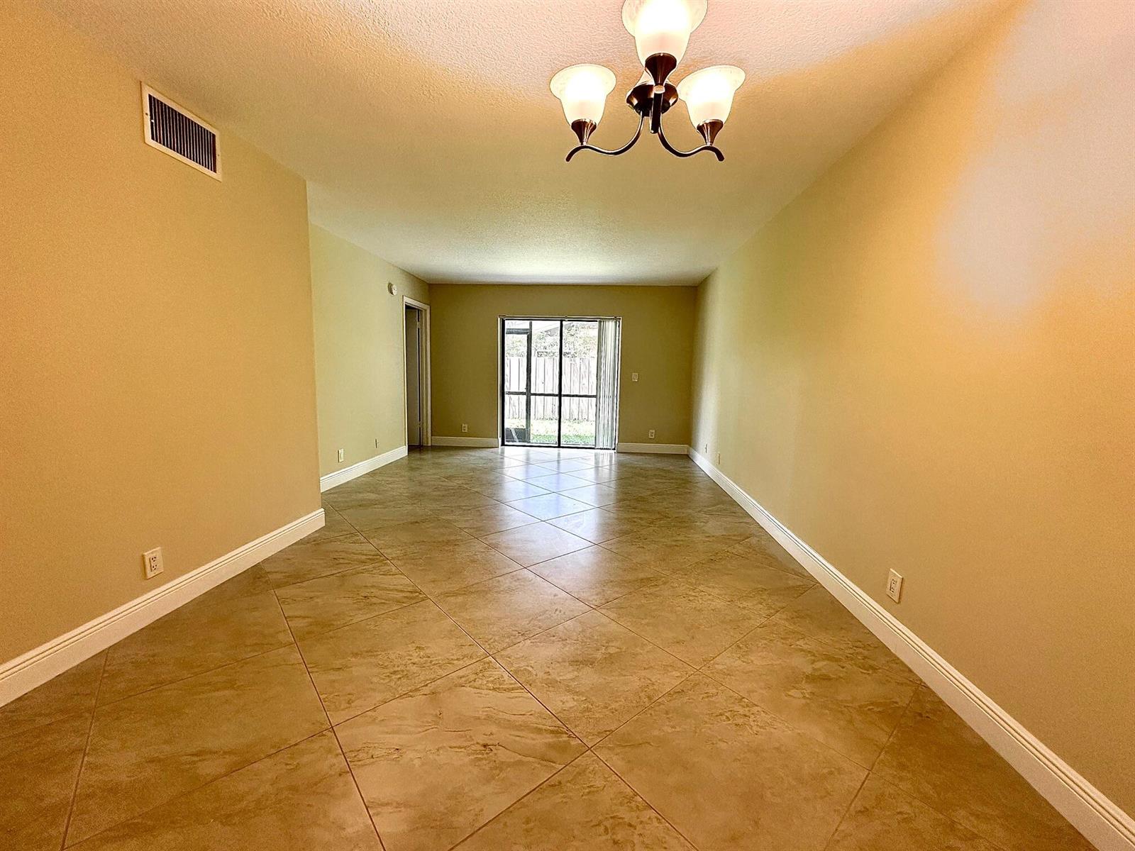 An empty room with tan walls, diagonal tile flooring, and a three-light chandelier — 21904 Lake Forest Circle # 101, Boca Raton FL 33433, BOCA RATON, FL