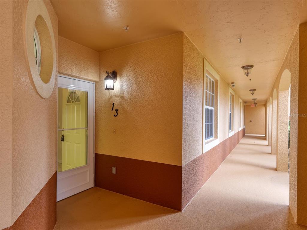 An exterior hallway with a yellow door marked 13, stucco walls, and arched columns — 150 L PAVIA BOULEVARD UNIT 13, VENICE, FL