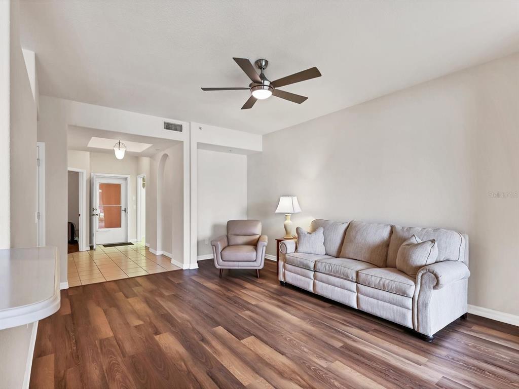 A living room features wood-look flooring, a ceiling fan, a sofa, and an armchair — 150 L PAVIA BOULEVARD UNIT 13, VENICE, FL