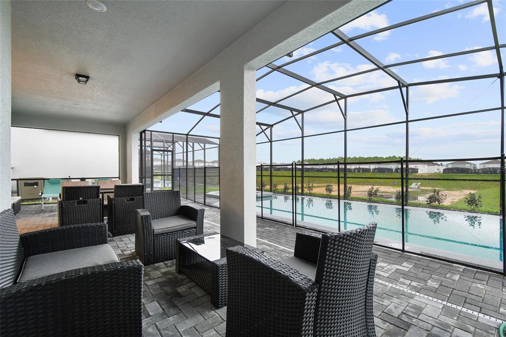 A covered patio with wicker furniture overlooks a screened-in swimming pool and a grassy yard — 3740 LANA AVENUE, DAVENPORT, FL