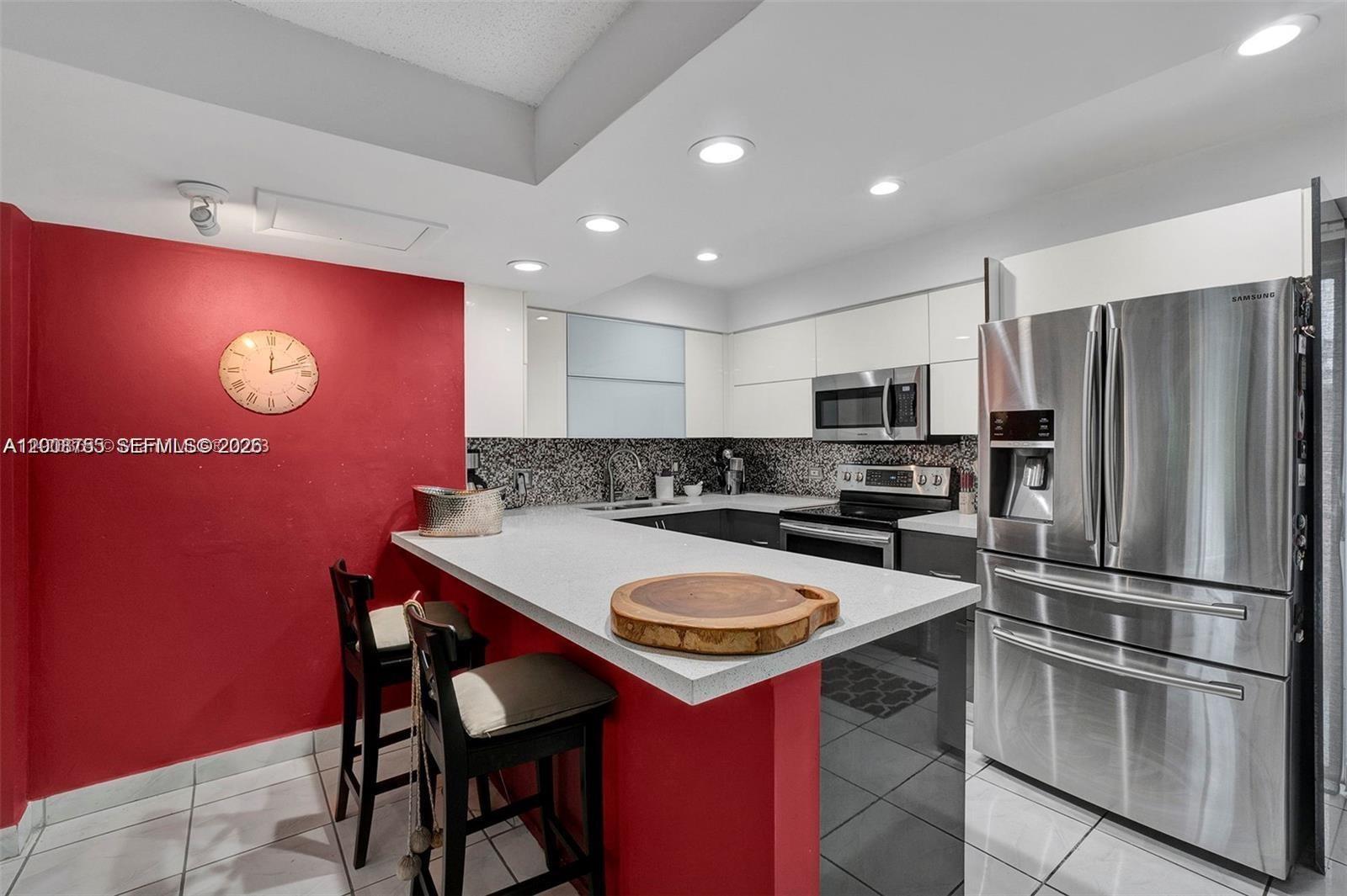 A kitchen features a red accent wall, white cabinetry, stainless steel appliances, and a breakfast bar — 6821 Brookline Dr # 6821, Hialeah FL 33015, HIALEAH, FL