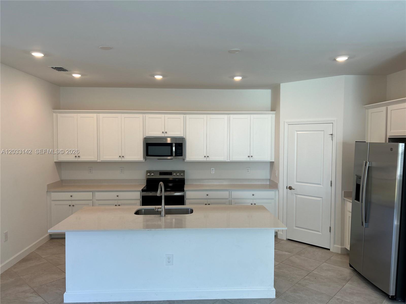 A kitchen features white cabinetry, stainless steel appliances, a center island, and tile flooring — 20483 Copperhead DR, Lehigh Acres FL 33936, LEHIGH ACRES, FL