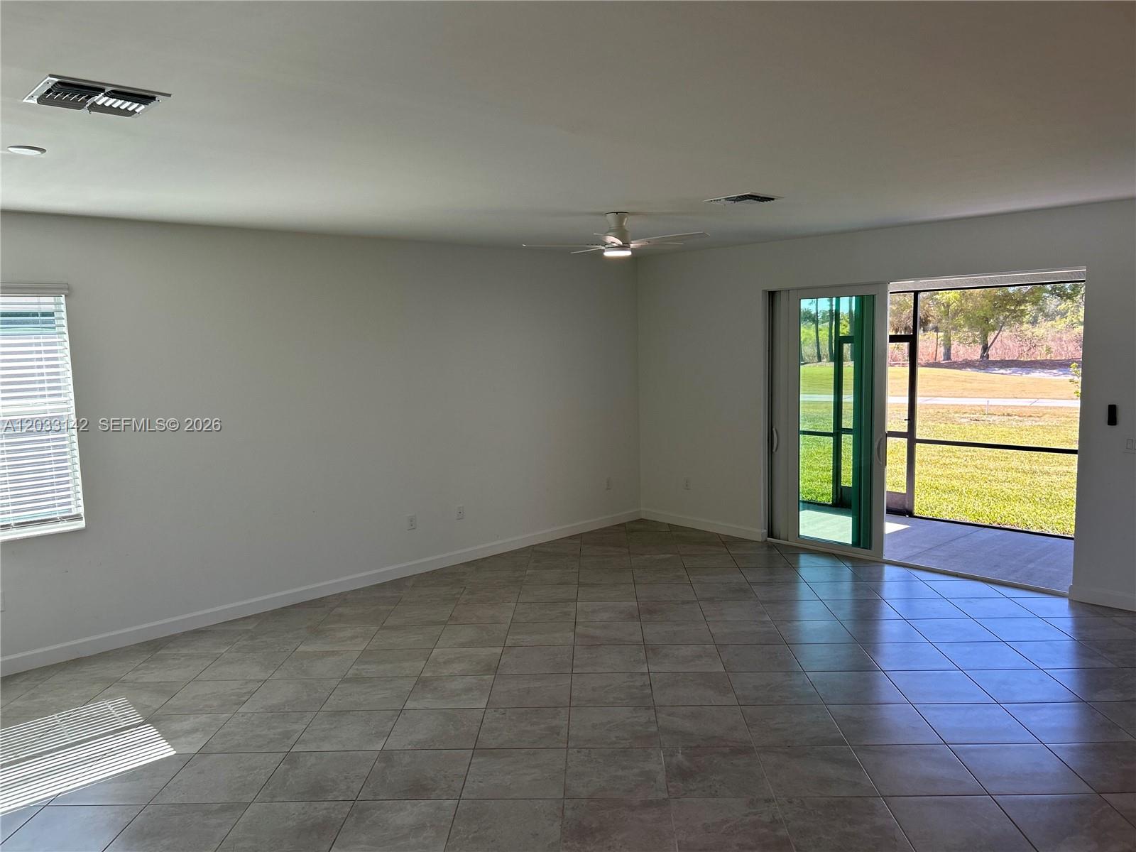 An empty room with light tile flooring, a ceiling fan, and sliding glass doors — 20483 Copperhead DR, Lehigh Acres FL 33936, LEHIGH ACRES, FL