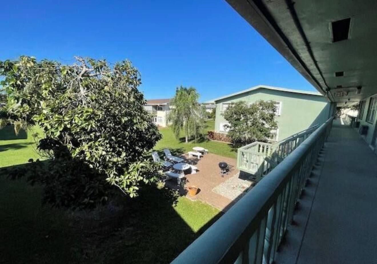 An elevated view from a balcony overlooking a grassy courtyard with patio furniture and trees — 66 Easthampton C # C, West Palm Beach FL 33417, WEST PALM BEACH, FL