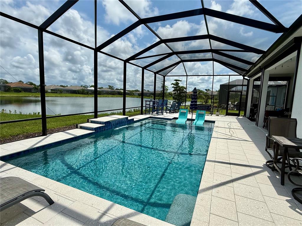 A screened-in swimming pool with a water feature overlooks a lake and neighboring houses — 9982 BRIGHT WATER DRIVE, ENGLEWOOD, FL