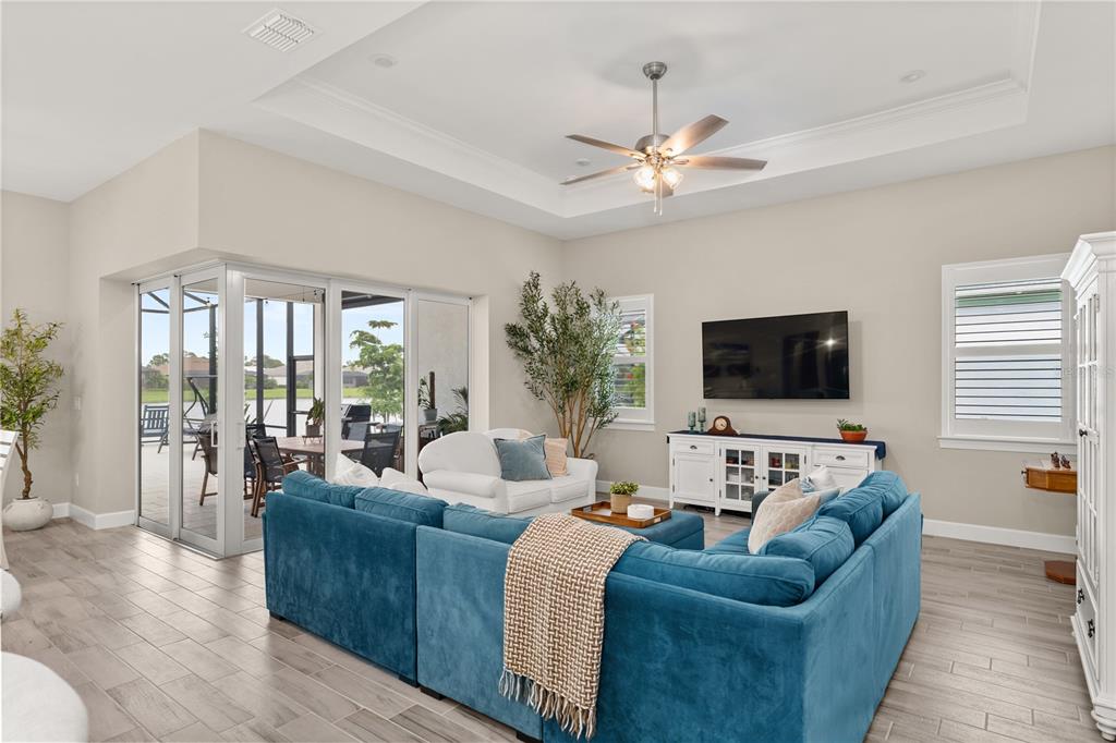 A living room features a blue sectional sofa, white media console, and sliding glass patio doors — 9982 BRIGHT WATER DRIVE, ENGLEWOOD, FL