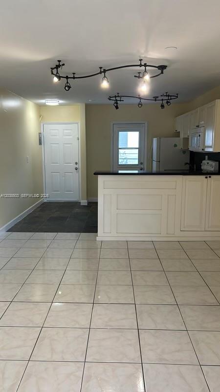 A kitchen with white cabinets and a breakfast bar opens to a tiled living area — 1600 NE 114th St # 208, Miami FL 33181, MIAMI, FL