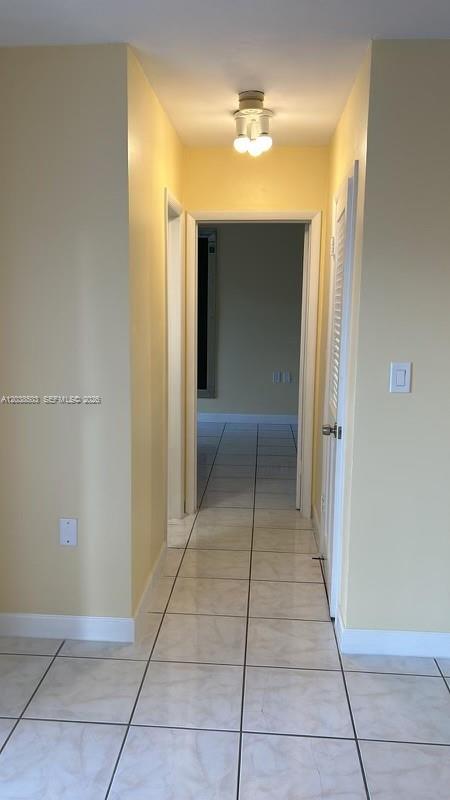 A hallway with light yellow walls and white tile flooring leads to an open doorway — 1600 NE 114th St # 208, Miami FL 33181, MIAMI, FL
