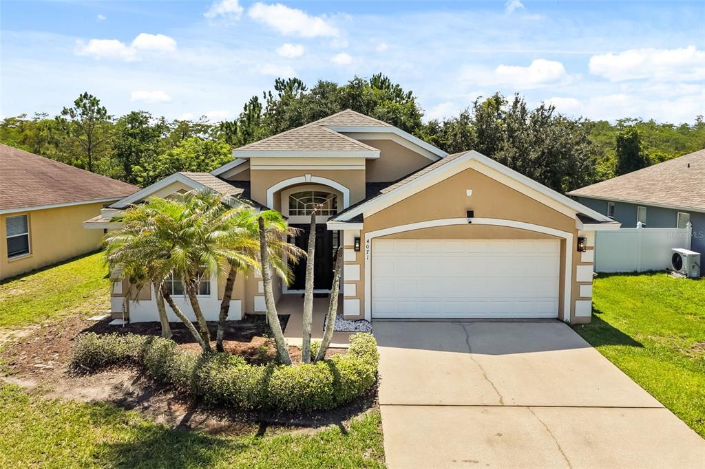 A tan single-story house with a white garage door, palm trees, and a landscaped yard — 4071 LONGWORTH LOOP, KISSIMMEE, FL