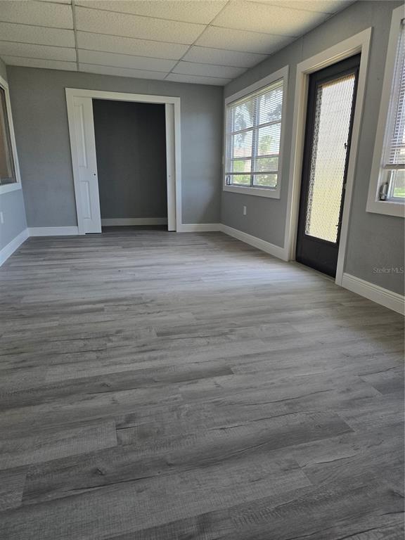 A room with gray walls, light wood-look flooring, a drop ceiling, and a glass door — 4836 ONYX LANE UNIT B, NEW PORT RICHEY, FL