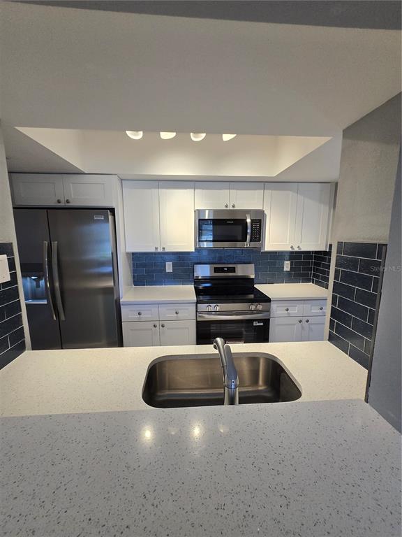 A kitchen features white cabinets, stainless steel appliances, a dark blue backsplash, and quartz countertops — 4836 ONYX LANE UNIT B, NEW PORT RICHEY, FL