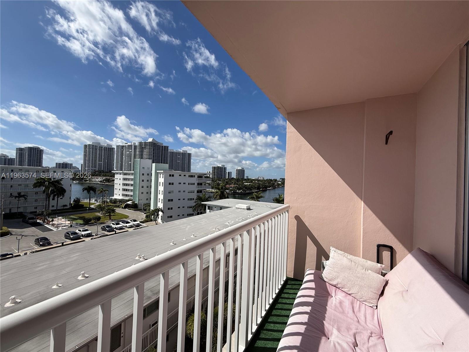 A balcony with a pink sofa overlooks a parking lot, nearby buildings, and a waterway — 3161 S Ocean Dr # 608, Hallandale Beach FL 33009, HALLANDALE BEACH, FL