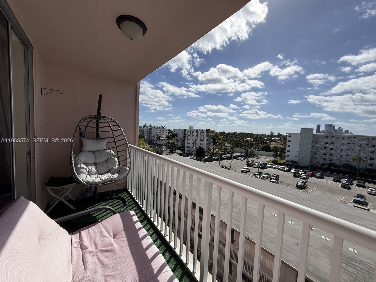 A balcony features a hanging egg chair, a pink lounge cushion, and a parking lot view — 3161 S Ocean Dr # 608, Hallandale Beach FL 33009, HALLANDALE BEACH, FL
