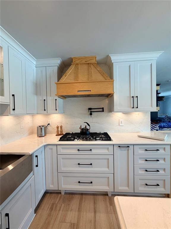 A kitchen features white cabinetry, a wooden range hood, and a marble-patterned backsplash — 3921 BELLE VISTA DRIVE E, ST PETE BEACH, FL