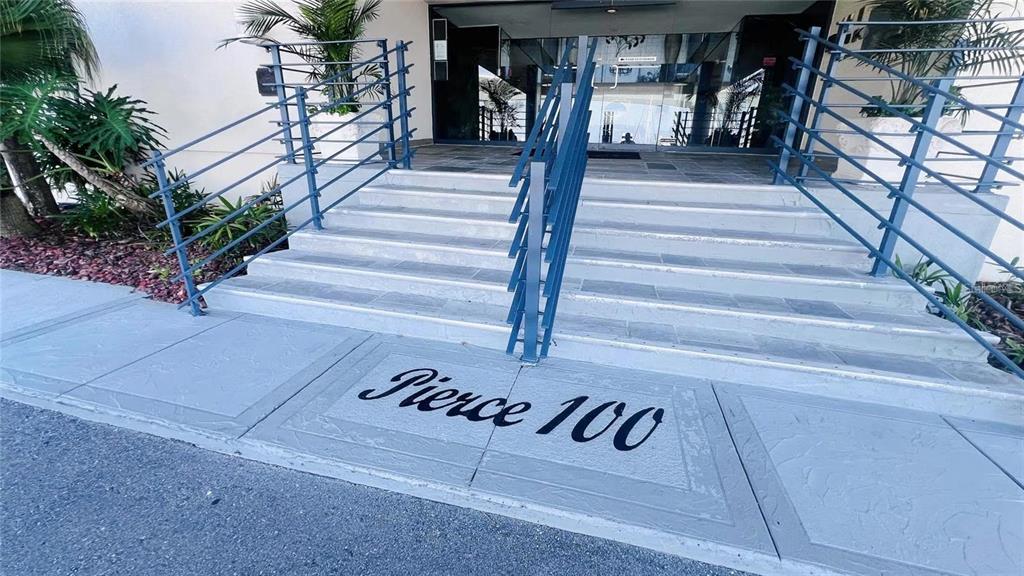 The exterior entrance of a building features concrete stairs with blue railings and signage — 100 PIERCE STREET UNIT 1001, CLEARWATER, FL