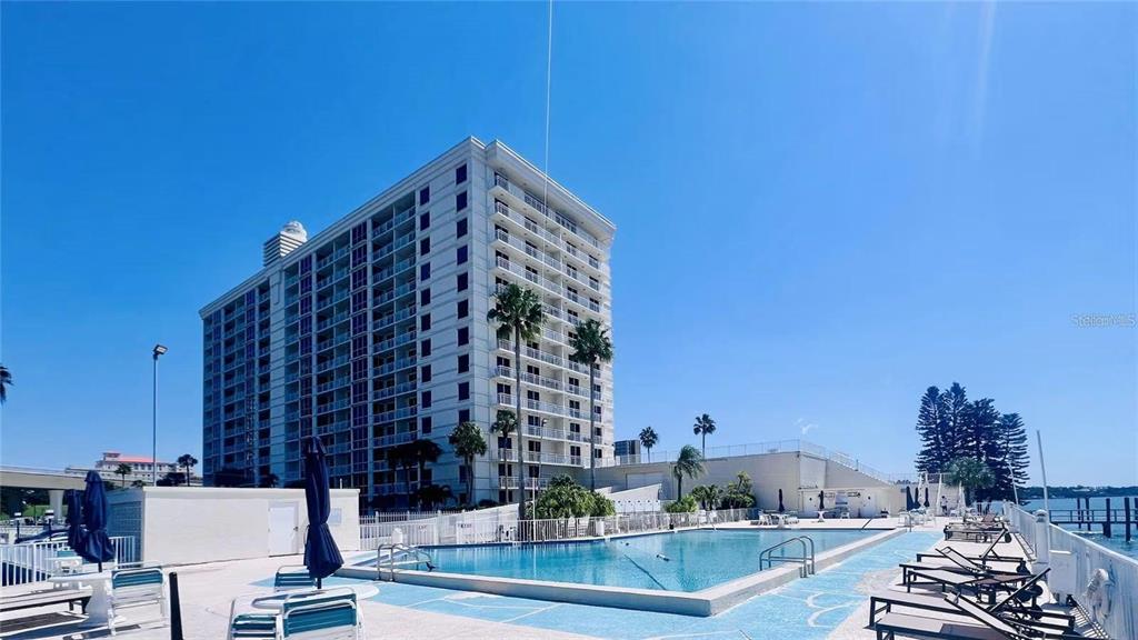 A tall residential building stands behind a swimming pool with lounge chairs on the deck — 100 PIERCE STREET UNIT 1001, CLEARWATER, FL